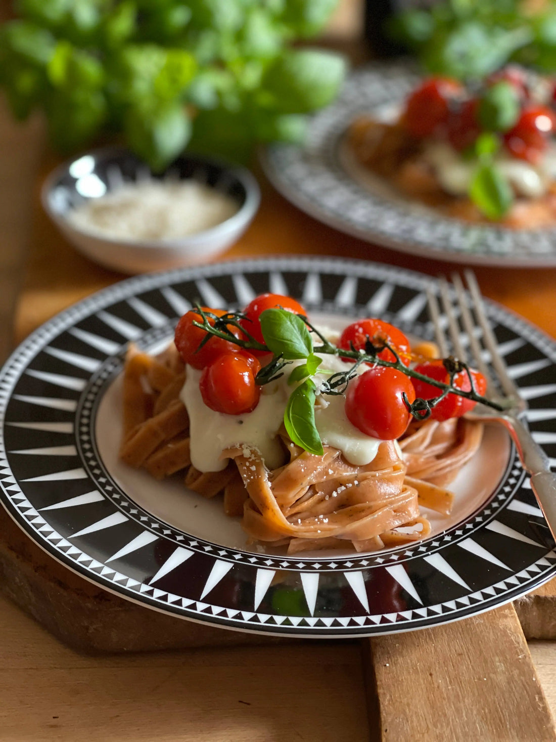 Fresh pasta with creamy sauce, cherry tomatoes, and basil on a patterned plate
