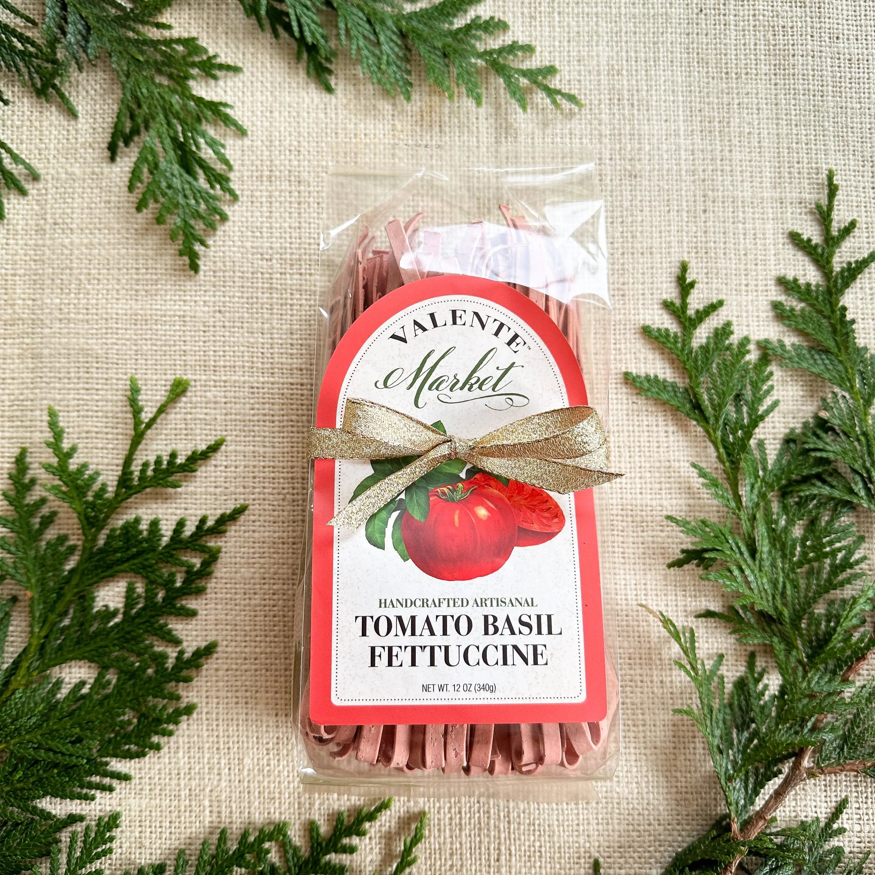 Packaged tomato basil fettuccine with gold ribbon, festive greenery, and burlap background