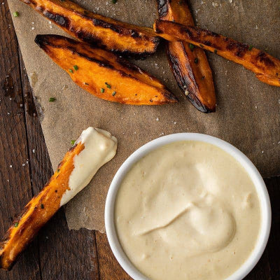 Grilled sweet potato wedges with a side of creamy dipping sauce on a wooden surface.