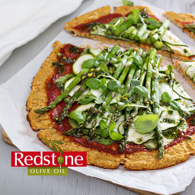 Vegetable pizza with asparagus and greens on a white surface, branded with Redstone Olive Oil.