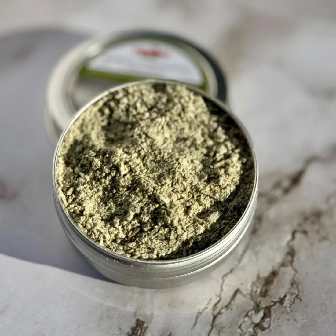 Closeup of dried basil herb in a round metal tin on a marble surface