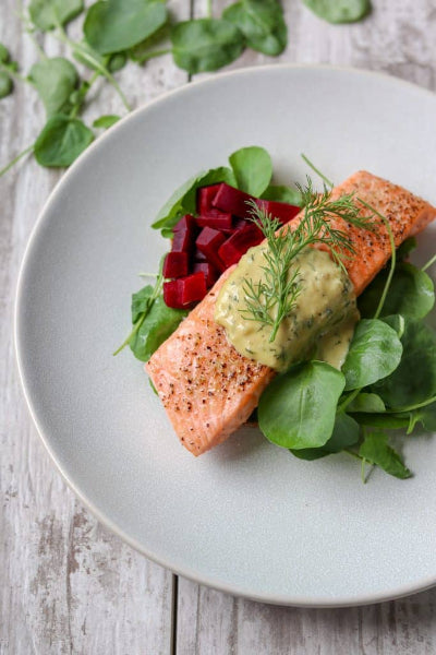 Grilled salmon with dill mustard sauce, beets, and fresh greens on a white plate