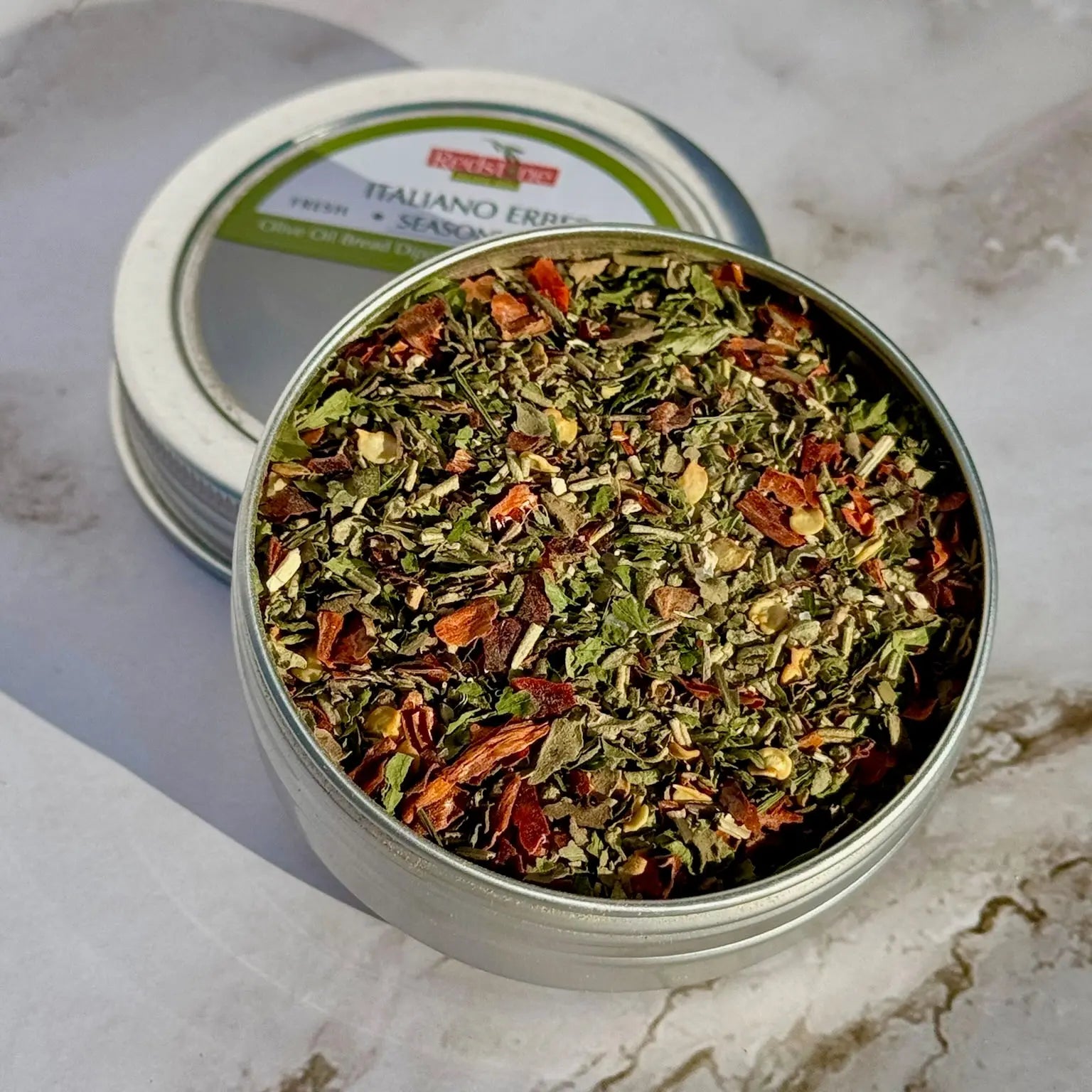 Closeup of Italian herb seasoning blend in an open tin on marble surface