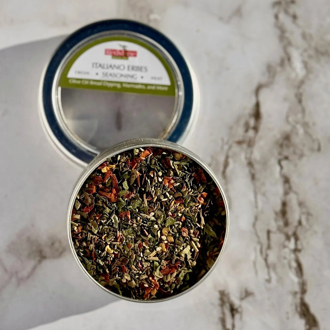 Open tin of Italiano herbs seasoning blend with colorful dried herbs on marble surface.