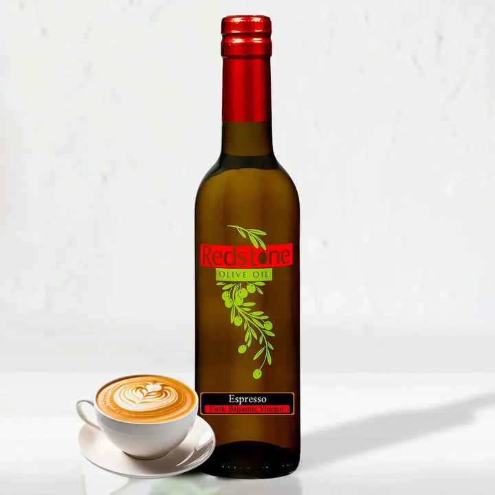 A glass bottle of Redstone Espresso Balsamic Vinegar with a dark cap, next to whole coffee beans and an espresso cup on a wood surface
