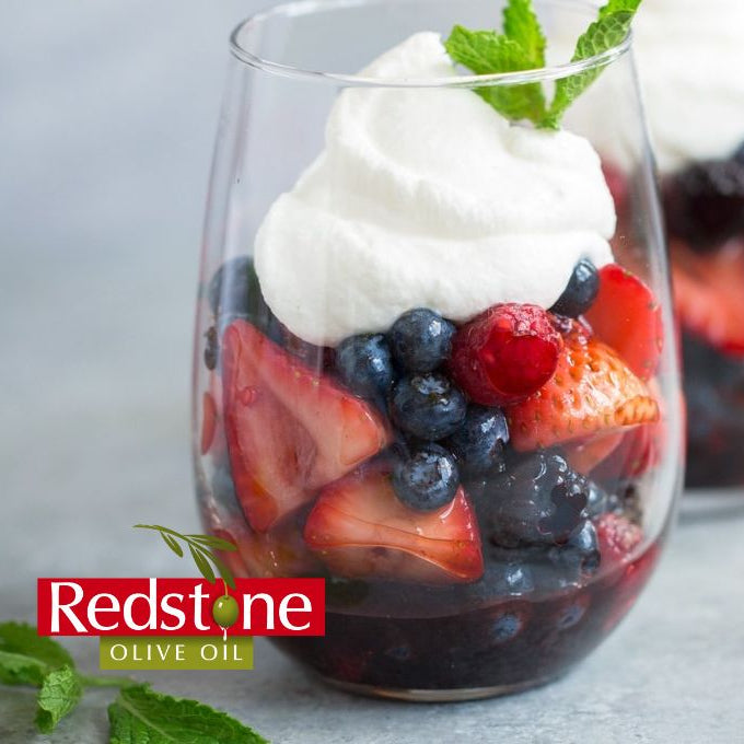 Two stemless wine glasses filled with a berry salad and whipped cream, with 'Redstone Olive Oil' branding.