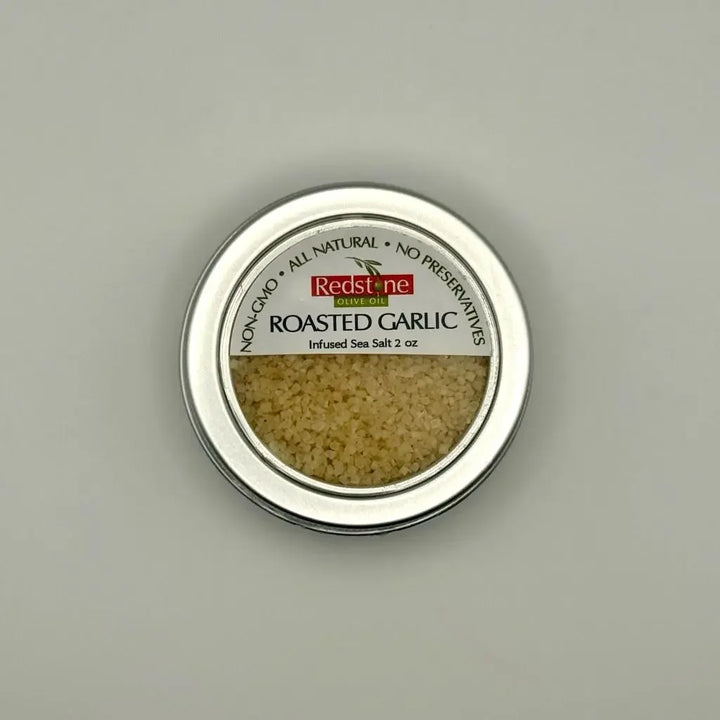 Overhead view of Redstone Roasted Garlic Sea Salt in silver round tin with clear lid — mellow caramelized roasted garlic finishing salt