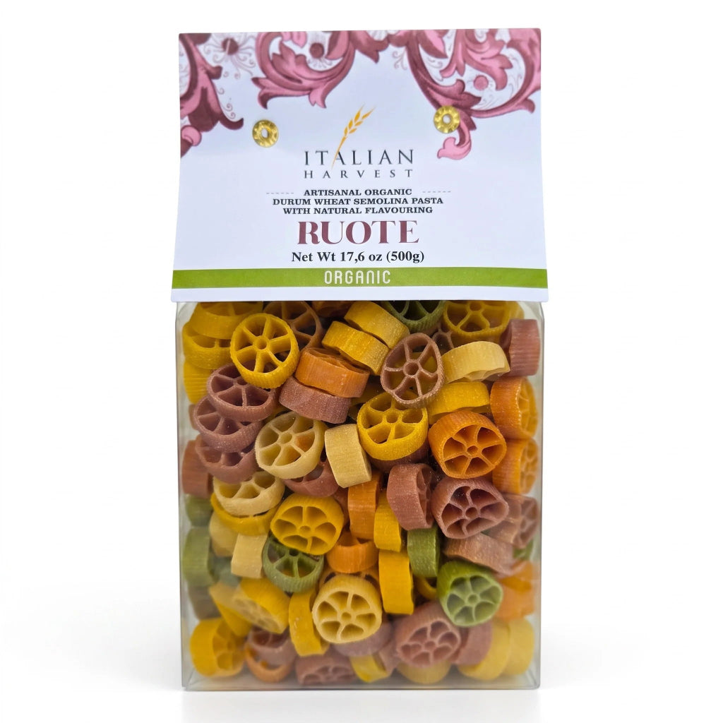 Italian Harvest Ruote Organic durum wheat semolina pasta in a clear plastic bag with a decorative white and pink header card, showing multicolored wheel-shaped pasta pieces inside.