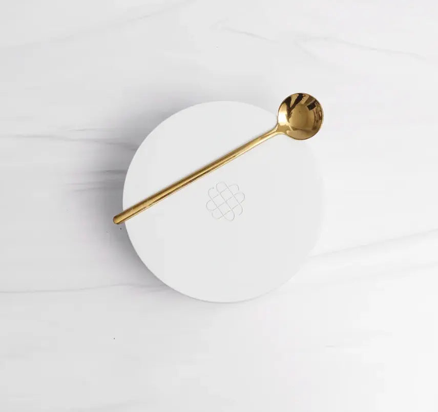 White ceramic salt cellar with a gold spoon on a marble surface