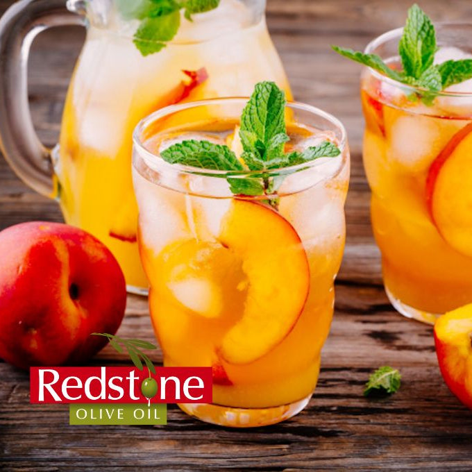 Peach iced tea with glasses and a pitcher on a wooden surface, featuring Redstone Olive Oil branding.