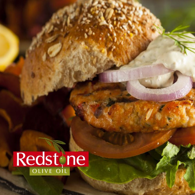 Salmon burger with lettuce, tomato, and onion on a bun with Redstone Olive Oil branding.