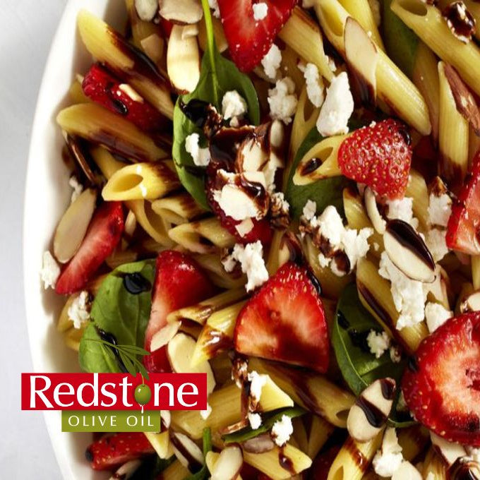 Pasta salad with strawberries and spinach on a white plate, featuring Redstone Olive Oil branding.