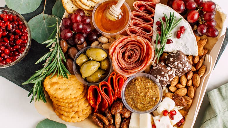 Charcuterie board with grapes, honey, olives, nuts, crackers, cheese, stone ground mustard.