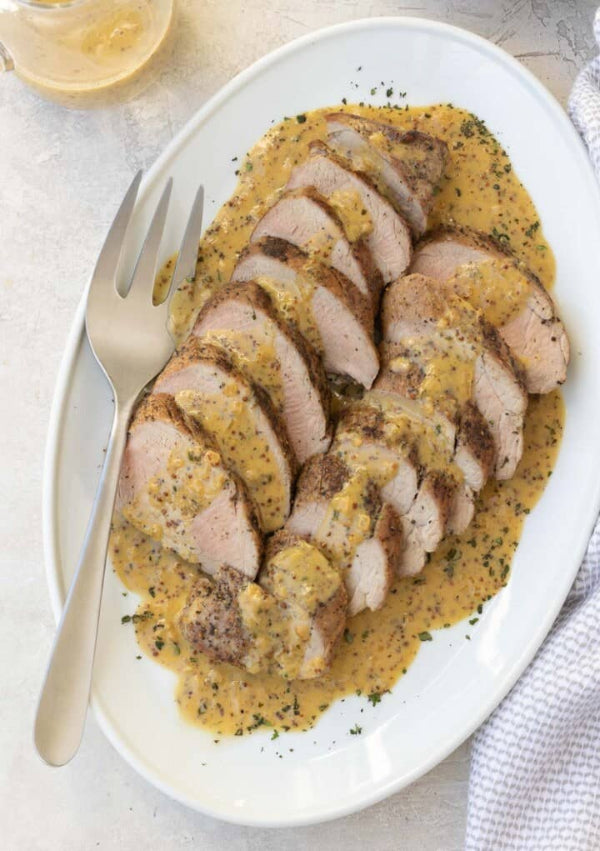Sliced roasted chicken breast topped with stone ground mustard sauce on a white plate