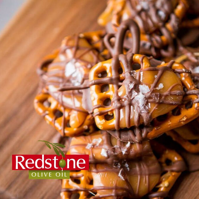 Chocolate-dipped pretzels on a wooden board with Redstone Olive Oil logo.