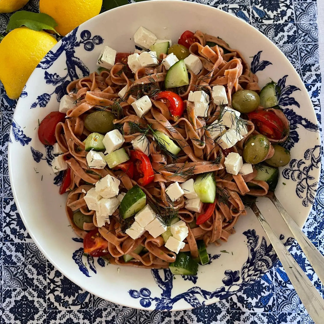 Mediterranean pasta salad with feta, olives, cucumber, tomato, and fresh herbs in a blue and white bowl