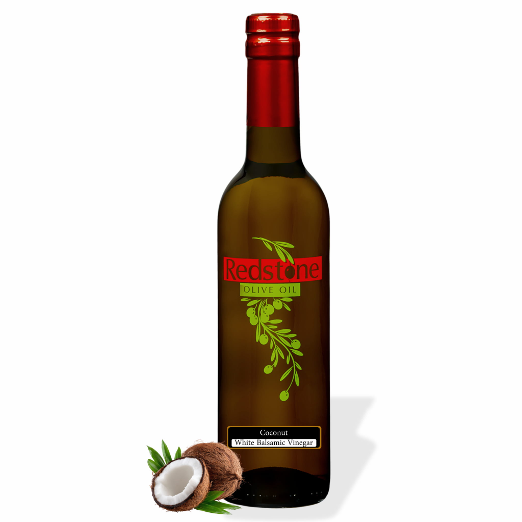 Bottle of Redstone Coconut White Balsamic Vinegar with a whole coconut, a cracked half, and palm leaves
