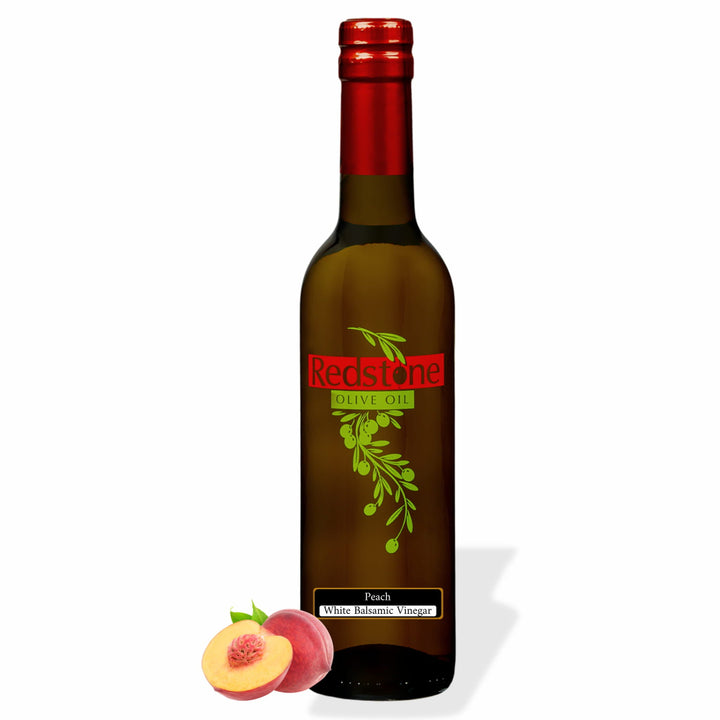 Bottle of Redstone Peach White Balsamic Vinegar with a whole and halved fresh peach