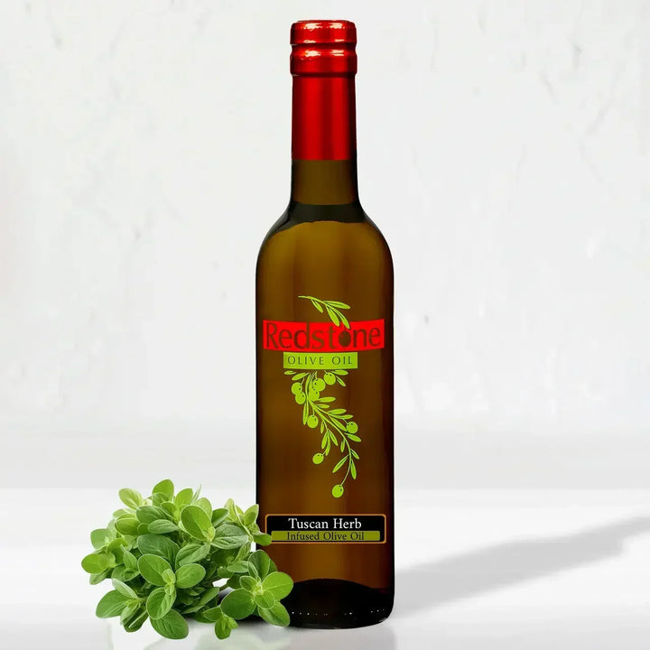 A bottle of Redstone Tuscan Herb Infused Olive Oil next to a fresh sprig of green Mediterranean herbs on a clean white surface