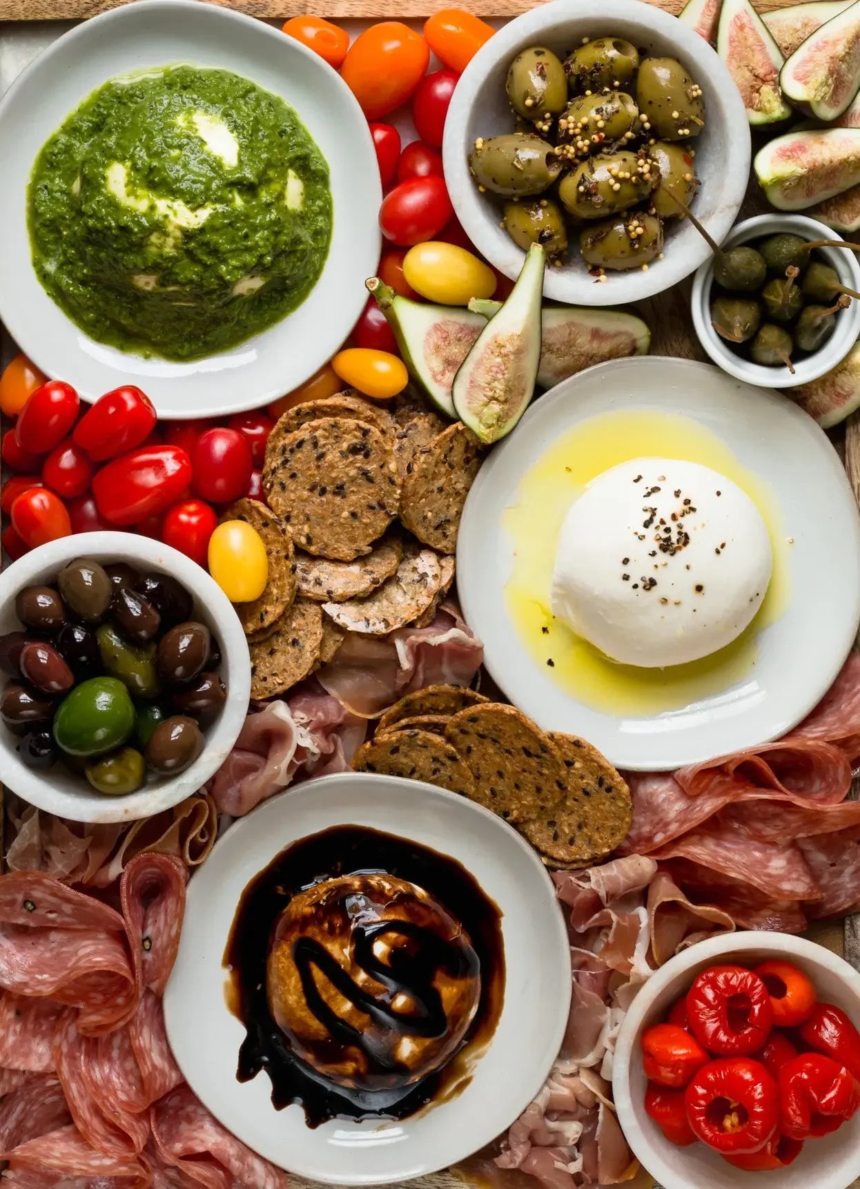 Charcuterie board with olives, figs, crackers, cured meats, burrata, pesto, balsamic drizzle, peppers